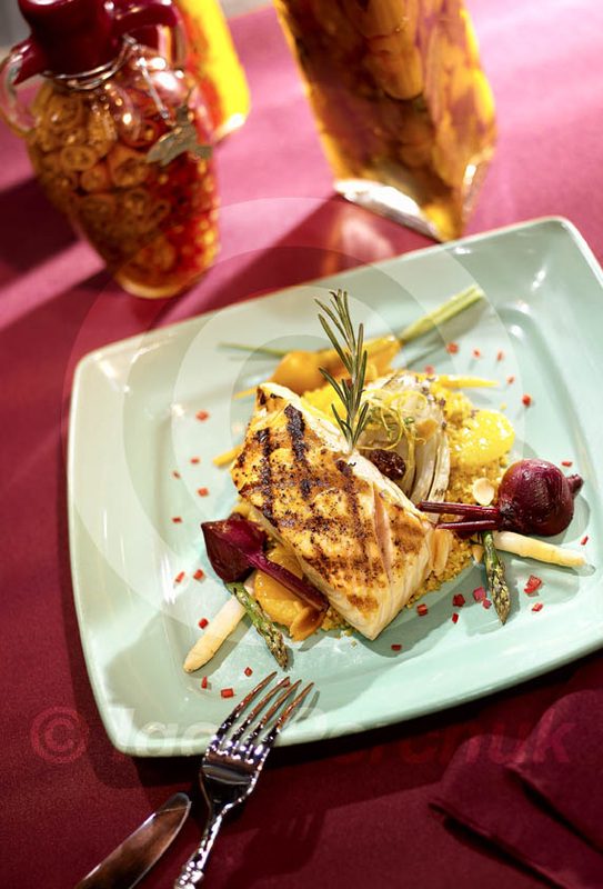 Grilled fish on a square plate at a red table setting