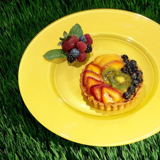 Fruit tart on a yellow plate set on fresh grass